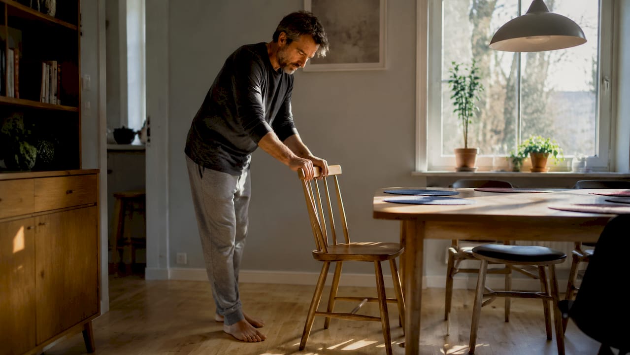 Een man schuift voorzichtig een stoel door de woonkamer.