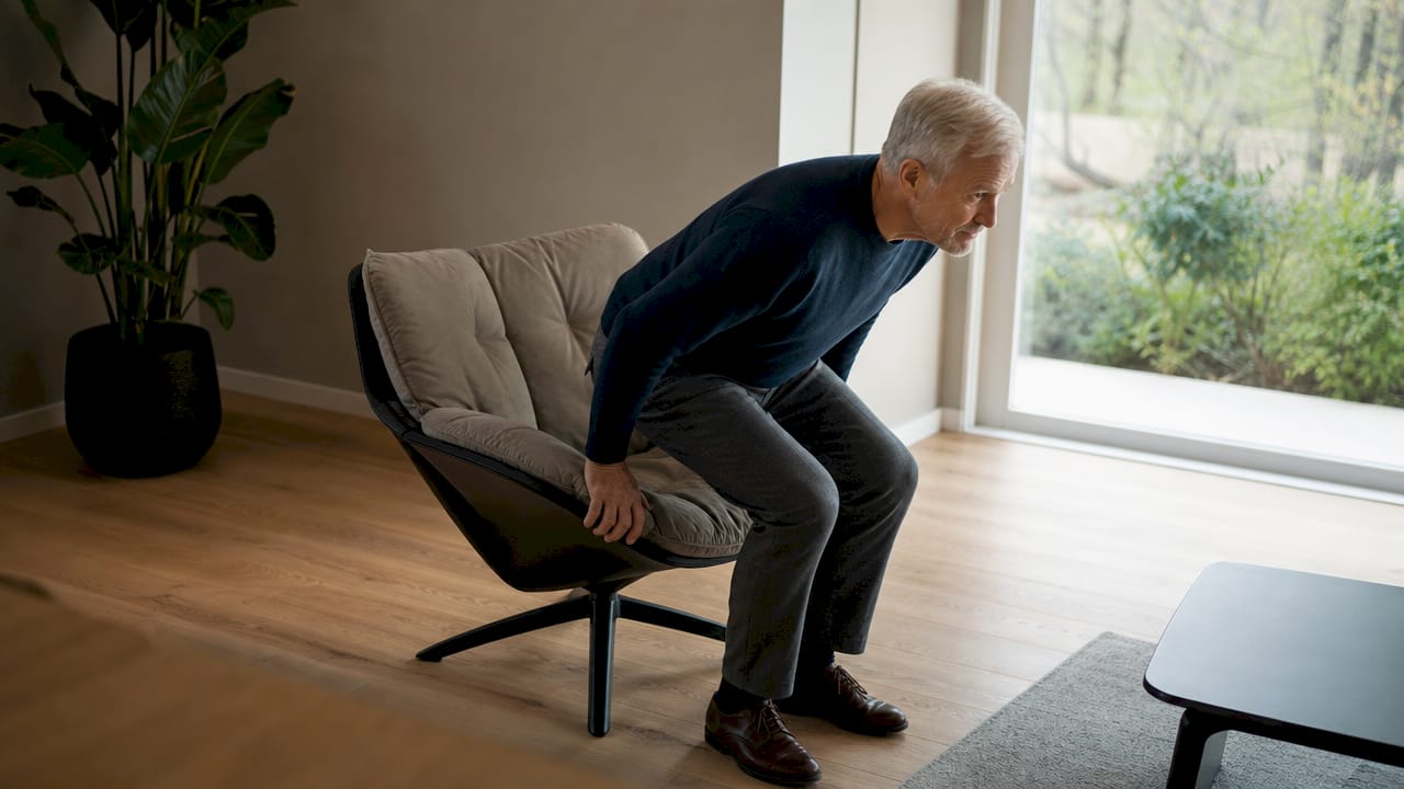 Een oudere man komt zonder hulp uit zijn stoel overeind in zijn eigen huis.