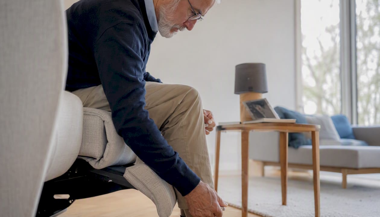 Een oudere man of vrouw die zijn of haar fauteuil even goed zet om lekker te kunnen zitten.